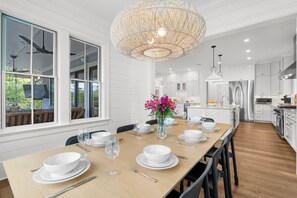 A modern kitchen with white cabinetry, a dining area with a wooden table set for four, and a large, woven pendant light. - Spectacular new rental home close to Ocean Course (Kiawah Island)