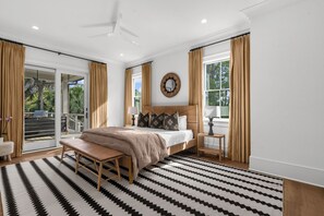 A bedroom with a bed, a bench, a bedside table, a mirror, and a view through a sliding door. - Spectacular new rental home close to Ocean Course (Kiawah Island)