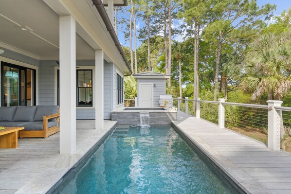 A swimming pool with a waterfall feature, a wooden deck, and a covered seating area with a sofa and table. - Spectacular new rental home close to Ocean Course (Kiawah Island)