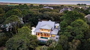 Ett modernt hus med en stor terrass och en swimmingpool, omgivet av tät vegetation och med utsikt över havet.