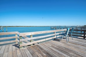 Eine hölzerne Pier, die sich in ruhiges Wasser erstreckt, mit einem wolkenlosen Himmel und einer in der Ferne erkennbaren Küste.