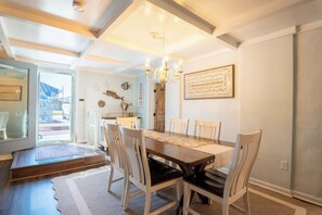 Ein Essbereich mit Holztisch, weißen Stühlen, einer Chandelierleuchte und Blick durch eine Glastür.