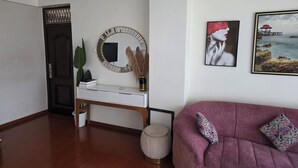 Un soggiorno moderno con un tavolo consolle bianco, uno specchio rotondo, un divano viola e un quadro incorniciato raffigurante una spiaggia.