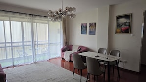 Un soggiorno con zona pranzo, un divano, un lampadario e un'ampia finestra con tende.