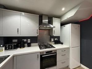 Una cocina moderna con armarios blancos, una campana extractora de acero inoxidable, un horno empotrado, un refrigerador y una estufa a gas.