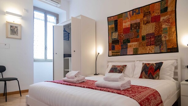 A bedroom with a bed, pillows, a quilt, a chair, a wardrobe, and a window. - Casa Sai (Rome)