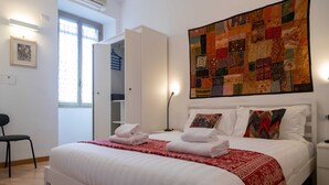 A hotel room with a large bed, a red and white patterned bedspread, a quilted wall hanging, and a white wardrobe. - Casa Sai (Rome)