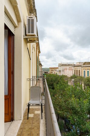 A balcony with a chair, an air conditioning unit, and a view of buildings. - Not Ordinary Apartment by Wonderful Italy (Noto)