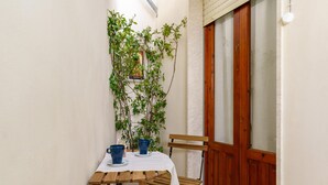 A small, enclosed outdoor dining area with a wooden table and chairs, a potted plant, and a door with frosted glass panels. - Not Ordinary Apartment by Wonderful Italy (Noto)