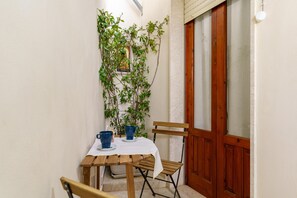 A small, enclosed outdoor dining area with a wooden table and chairs, a potted plant, and a door with frosted glass panels. - Not Ordinary Apartment by Wonderful Italy (Noto)