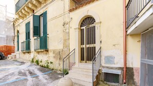 A building with a staircase leading to a door, a small garden area, and a parked car. - Not Ordinary Apartment by Wonderful Italy (Noto)