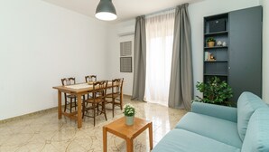 A living room with a dining table, chairs, a sofa, a small table with a plant, a bookshelf, and a hanging light fixture. - Not Ordinary Apartment by Wonderful Italy (Noto)