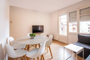 A modern living room with a round dining table, white chairs, a grey sofa, and a television on the wall. - TUA44PAA1129 - Carrer de Pau Alsina 57 (Barcelona)