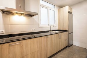 A kitchen with wooden cabinets, a stainless steel range hood, a window above the sink, and a built-in dishwasher. - TUA44PAA1129 - Carrer de Pau Alsina 57 (Barcelona)