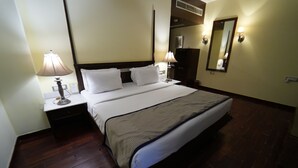 A hotel room with a large bed, two bedside tables with lamps, a dresser, a mirror, and a wooden floor.