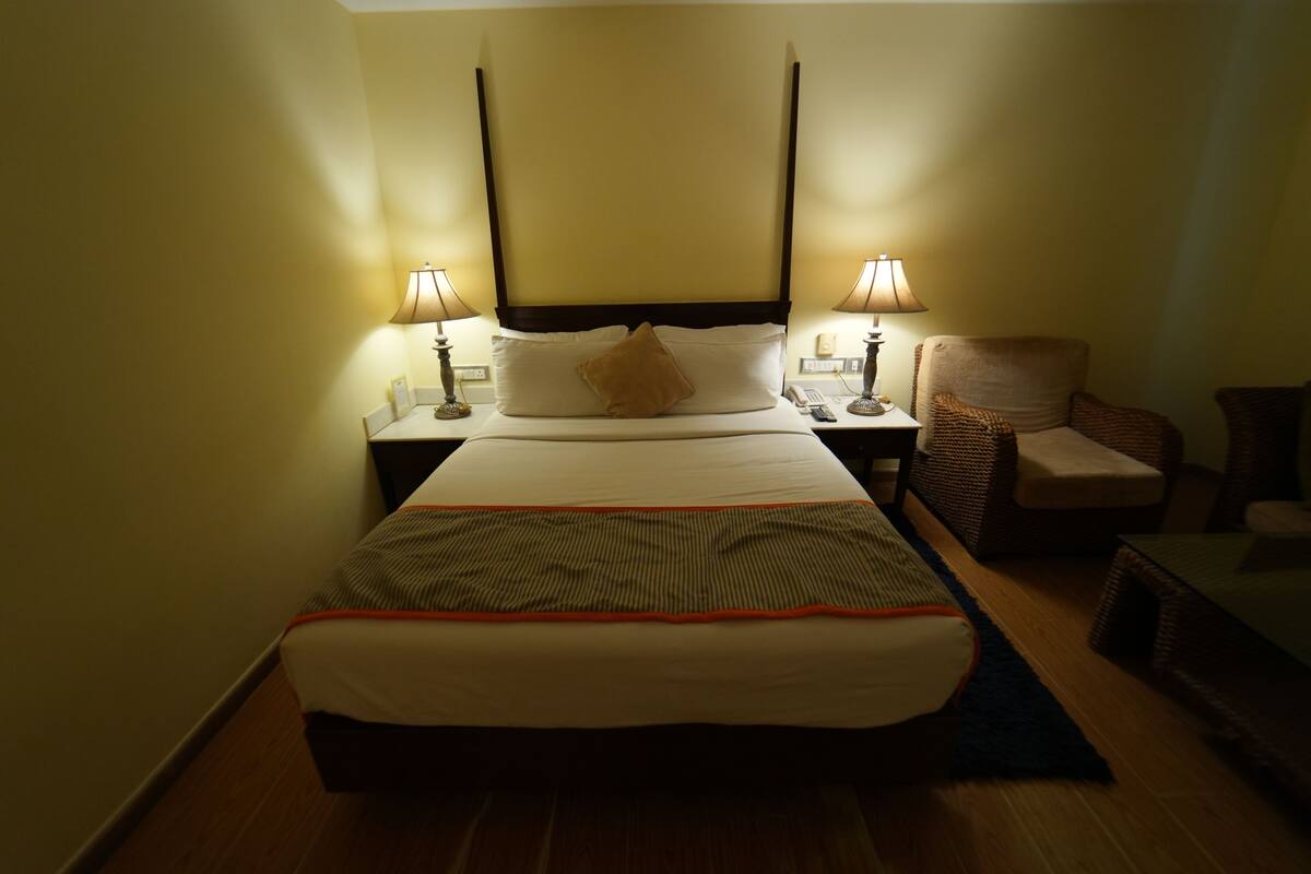 Una habitación de hotel con una cama, dos lámparas de noche, una silla y una mesita de noche.