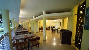 A spacious indoor area with multiple tables and chairs, a high ceiling, and a view of the outdoors.