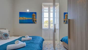 A hotel room with a bed, a door leading to a balcony, and a painting of a coastal scene.