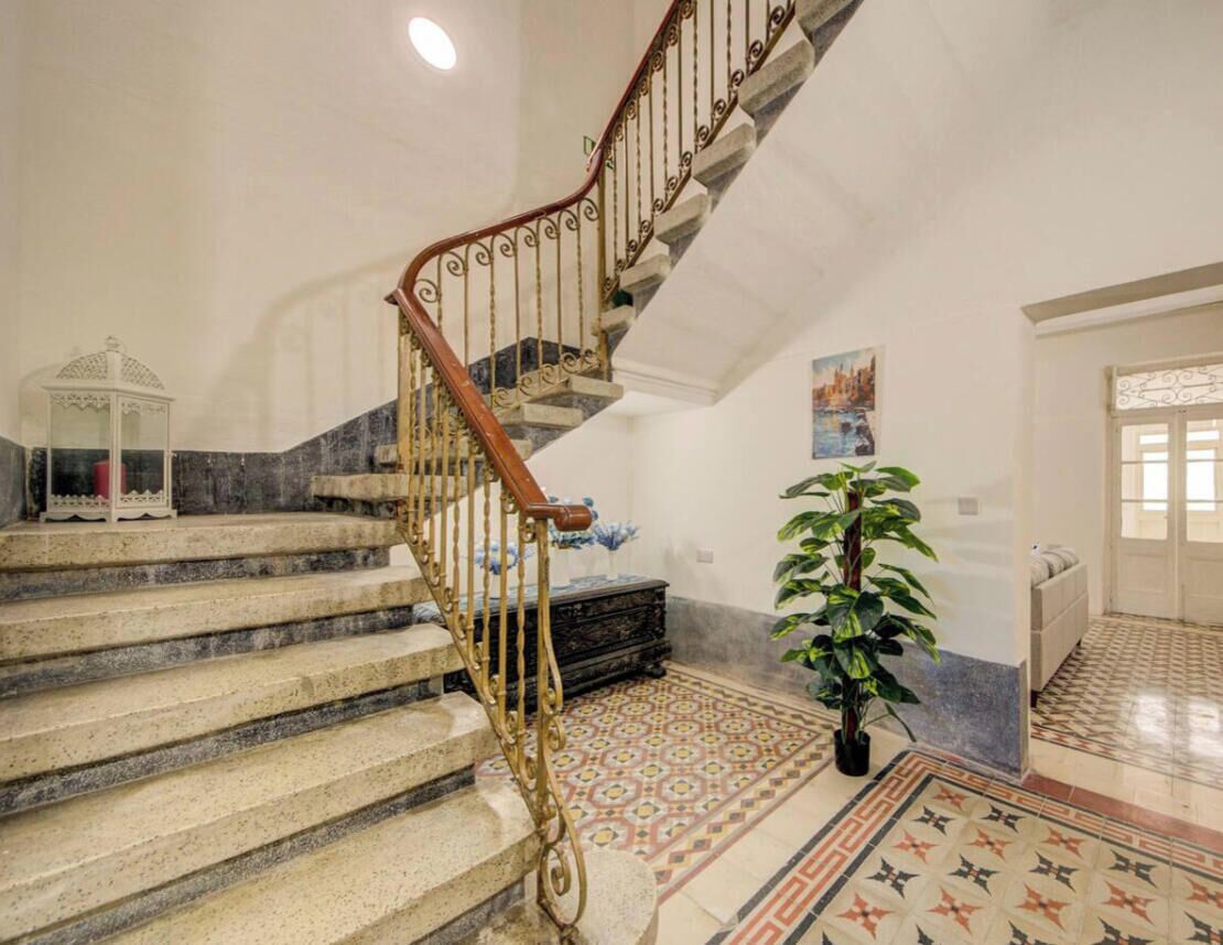 Un escalier orné de rampes en métal décoratives, un sol à motifs et une plante en pot.