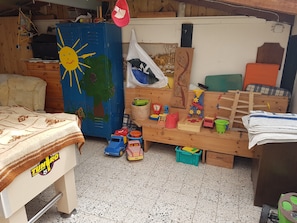 Une salle de jeux pour enfants avec des jouets, un meuble bleu orné d’un motif représentant un soleil, un lit et un banc en bois.