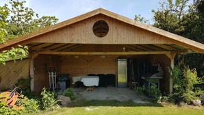Eine Holzhütte mit einer überdachten Veranda, einem Tisch mit Stühlen, einem Kühlschrank und einem kleinen Tisch mit Gegenständen darauf.