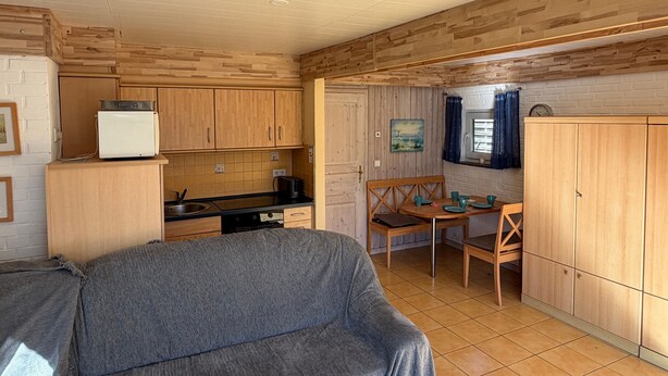 Eine kleine Küche mit Holzschränken, einem Esstisch mit Stühlen und einem grauen Sofa.