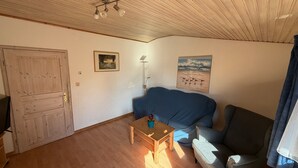 Ein Zimmer mit Holztür, einem blauen Sofa, einem kleinen Holztisch und zwei Wandleuchten.