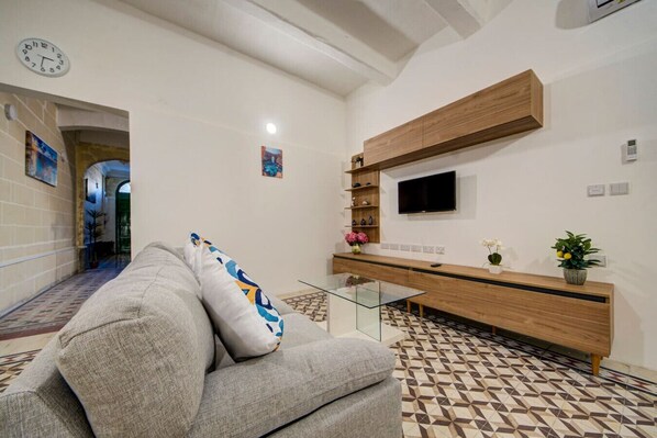 A living room with a sofa, a coffee table, a TV mounted on the wall, and a patterned floor.