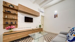 Ein modernes Wohnzimmer mit Fernseher, Holzregalen, einem Glastisch und einem Musterboden.