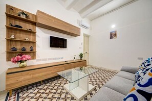 A modern living room with a TV, wooden shelves, a glass coffee table, and patterned flooring.