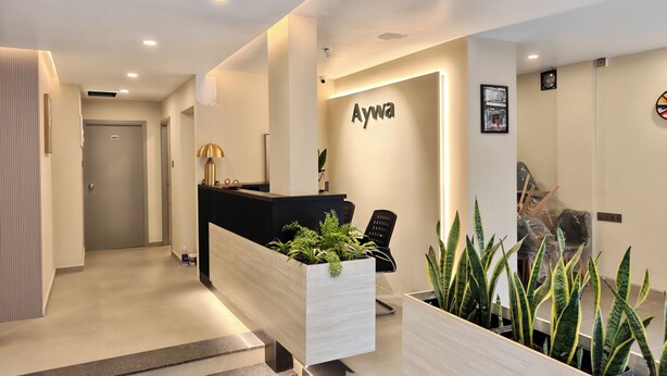A reception area with a reception desk, a nameplate, a plant, and a staircase. - AYWA Hotels (Kanayannur)