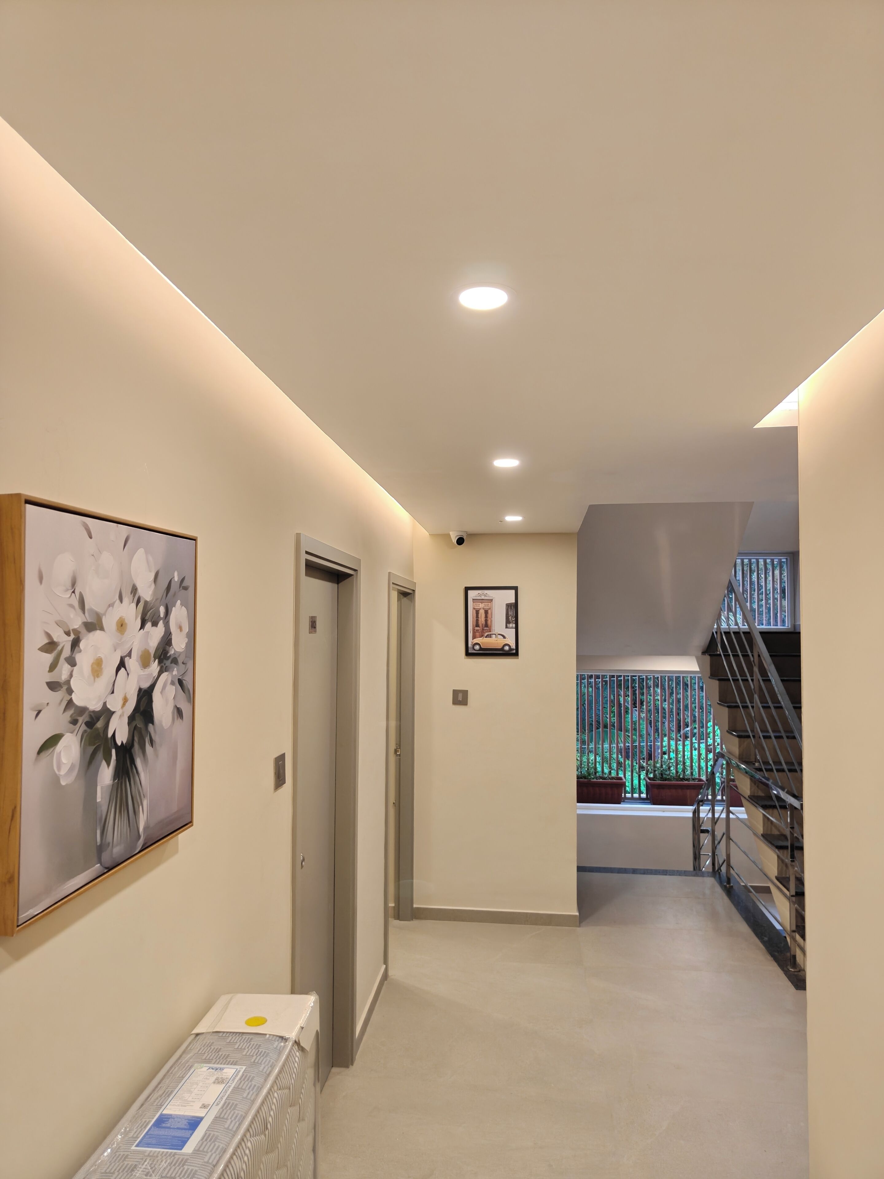 A hallway with a painting of flowers, a door, a framed picture, and a staircase.