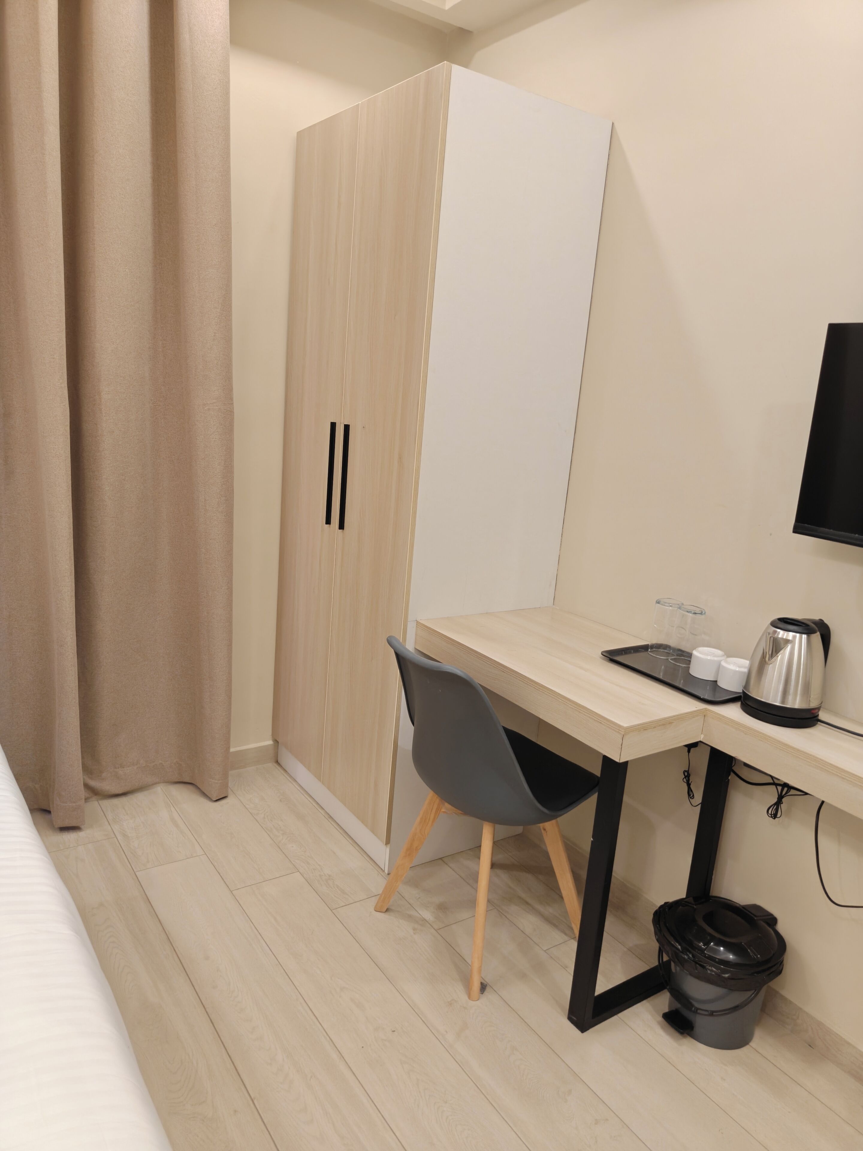 Une chambre d’hôtel comprenant un lit, un bureau avec une chaise, une armoire, un téléviseur, une machine à café et une poubelle.