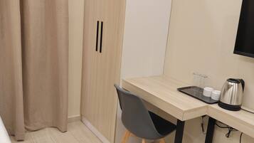 Une chambre d’hôtel comprenant un lit, un bureau avec une chaise, une armoire, un téléviseur, une machine à café et une poubelle.