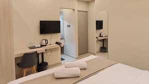 A hotel room with a bed, a desk with a chair, a television, a mirror, and an air conditioning unit. - AYWA Hotels (Kanayannur)