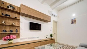 A modern living room with a glass coffee table, a grey sofa, wooden shelves, and a mounted TV. - Private Room in Hamrun with Shared Kitchen (Hamrun)