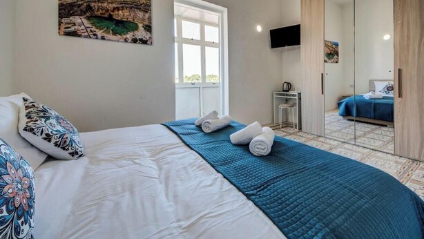 A bedroom with a bed, a window, a mirror, and a painting on the wall. - Private Room in Hamrun with Shared Kitchen (Hamrun)