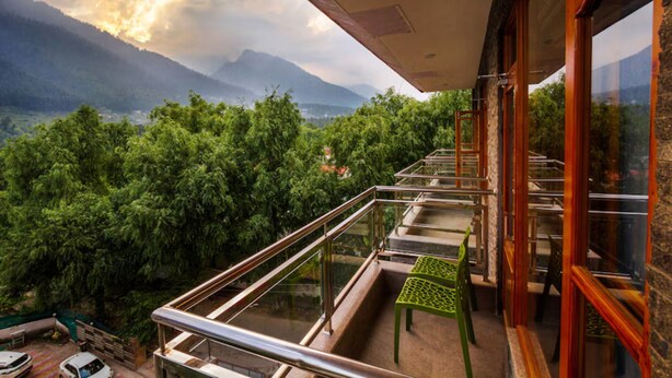 Ein Balkon mit Blick auf Berge und Bäume, mit Glastrennwand und einem grünen Stuhl.