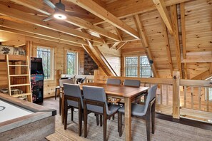A wooden interior with a dining table, chairs, a pool table, and a video game machine.