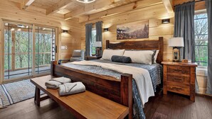 Camera da letto in una baita di legno, con un letto grande, comodini, una panca e vista sulla foresta.