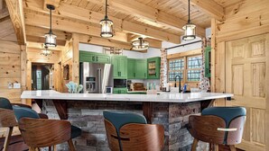 Una cucina con travi in legno, mobili verdi, una grande isola con sgabelli da bar e illuminazione a sospensione.