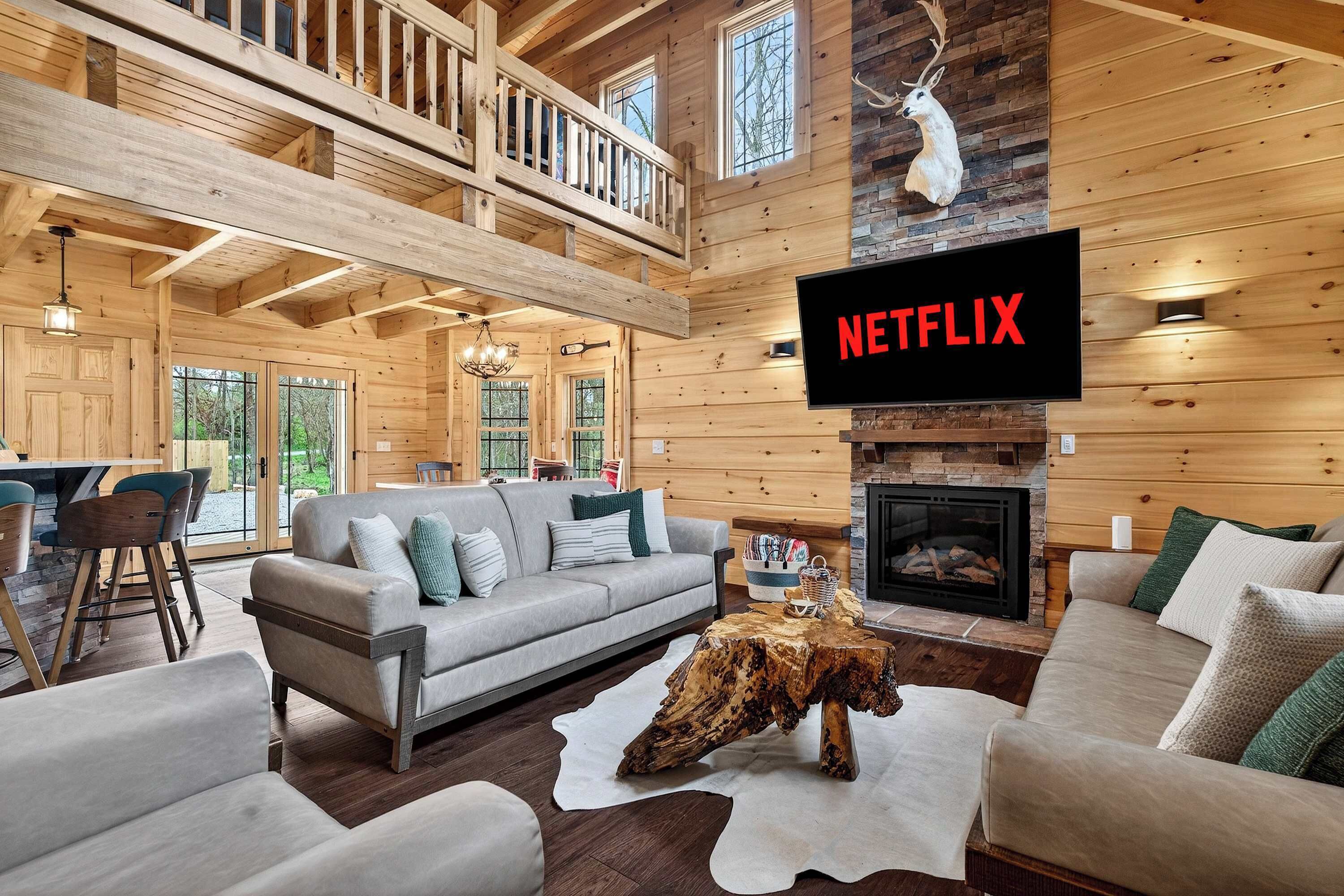 Uma sala de estar espaçosa com lareira, TV fixada exibindo 'NETFLIX' e teto de madeira.
