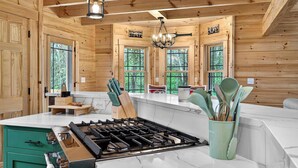 Interno di una baita in legno con cucina, caratterizzata da un piano cottura a gas, mobili in legno e ampie finestre.
