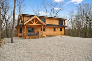 A wooden cabin with a porch, a covered entryway, and a gravel driveway.