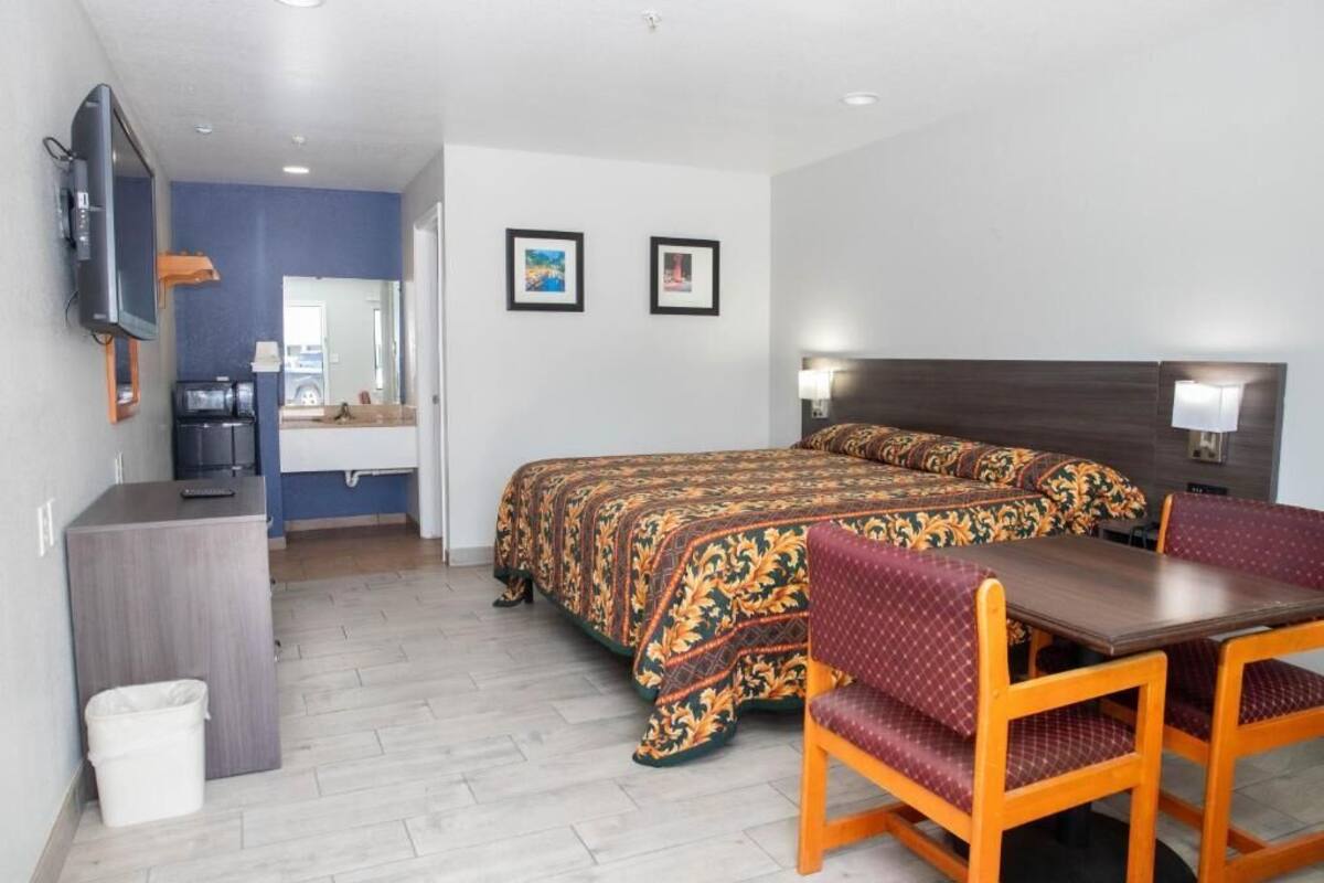 Habitación de hotel con cama, escritorio, silla, televisor y dos cuadros en la pared.