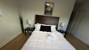 Una cama bien hecha con ropa blanca, dos mesitas de noche con lámparas, un cuadro enmarcado en la pared y un suelo de madera.