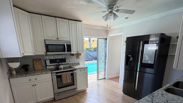 Una cocina con gabinetes blancos, microondas, horno, refrigerador y ventilador de techo.