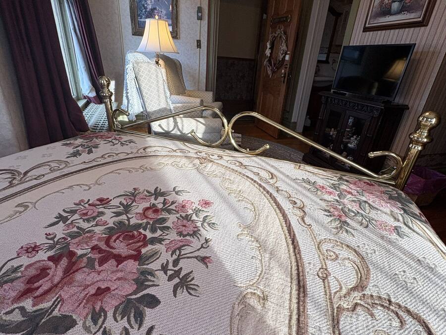 A bedroom with a bed, a lamp, a television, and a door leading to another room.