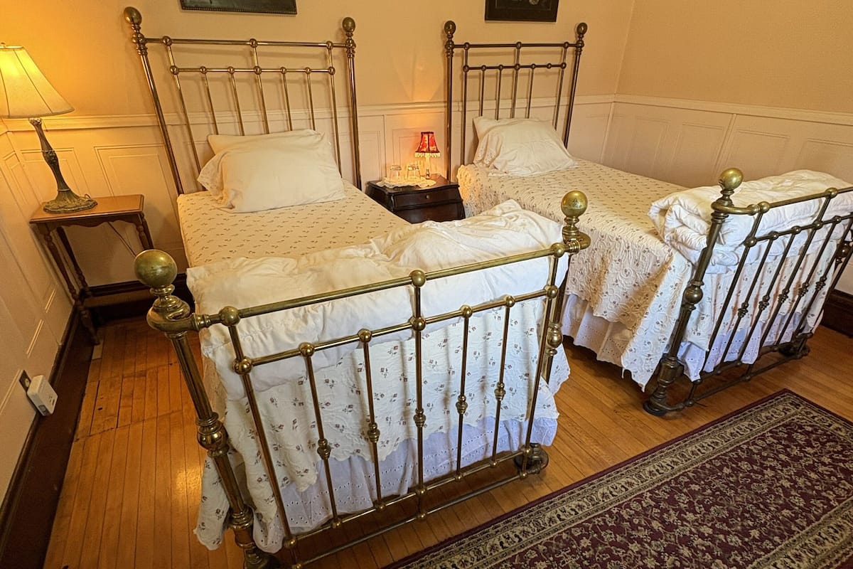 A room with two beds, a nightstand, a lamp, and a rug.