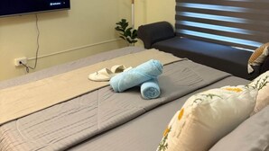 A hotel room with a bed, a TV mounted on the wall, a window with blinds, and a small plant on a shelf. - Modern Comfort at Avida Towers Riala (Cebu City)